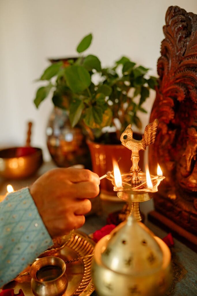 A close-up of a hand lighting a brass oil lamp during Diwali with a Ganesha statue and potted plants.